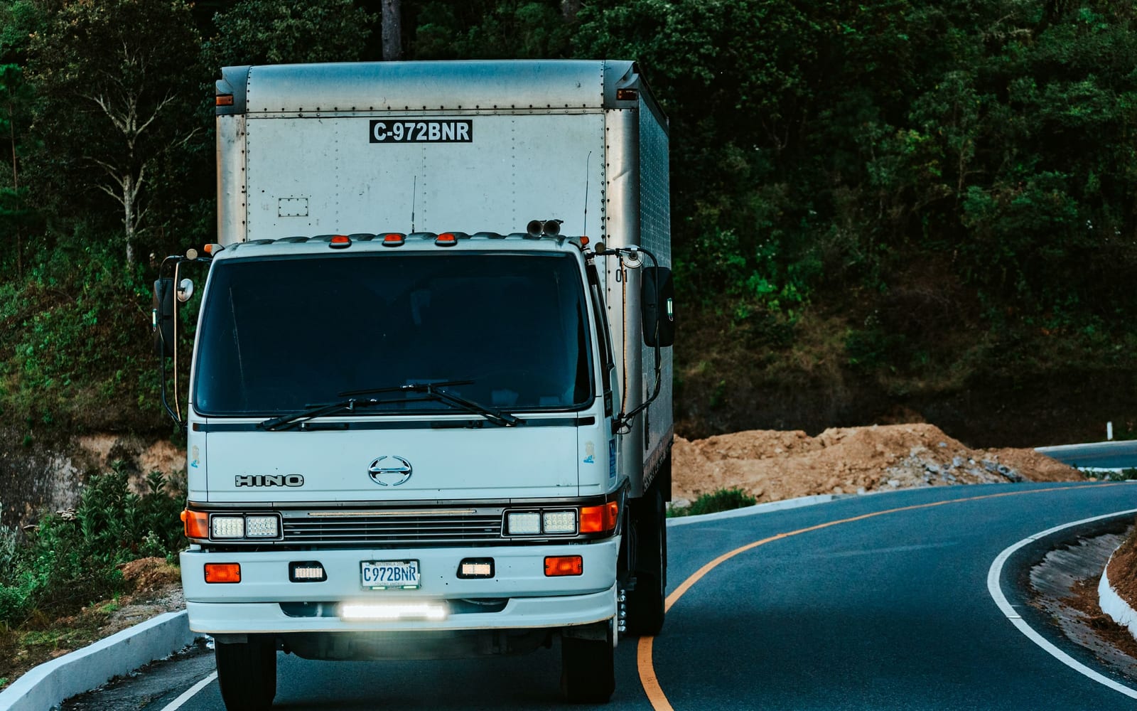 A service truck on a winding road, headlights on, heading out to a job