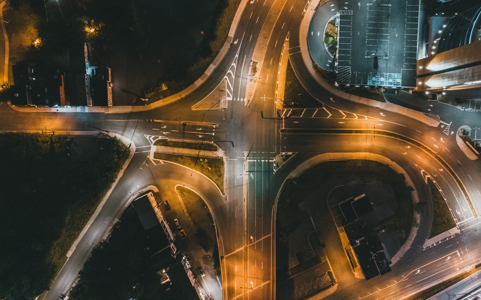 An aerial night view of a road junction where several lit routes converge into ordered lanes