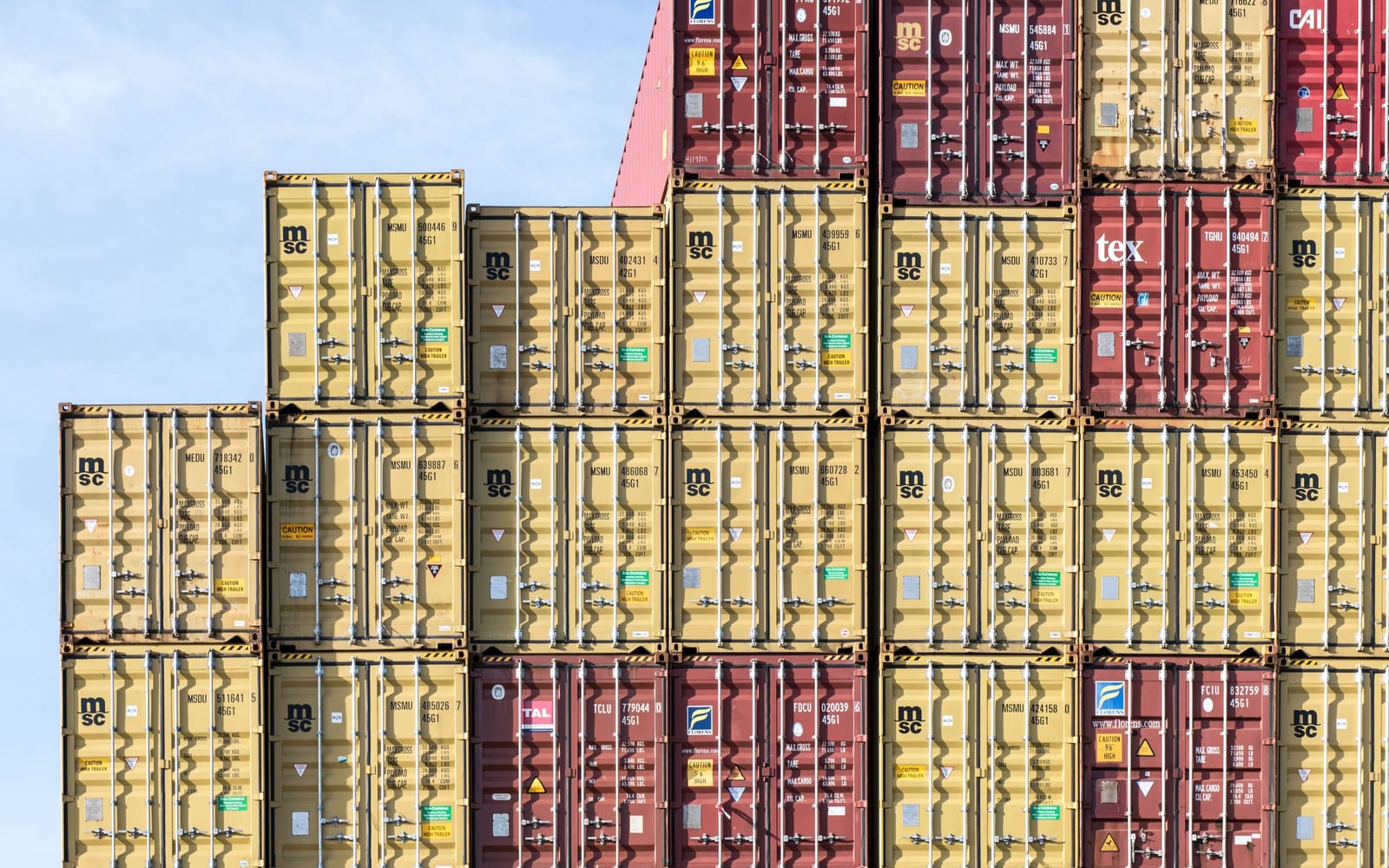 A wall of shipping containers stacked in even layers at a port terminal