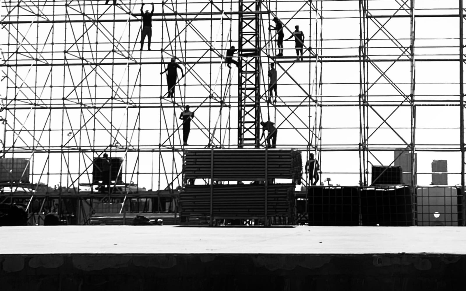 Workers spread across scaffolding, silhouetted against a pale sky