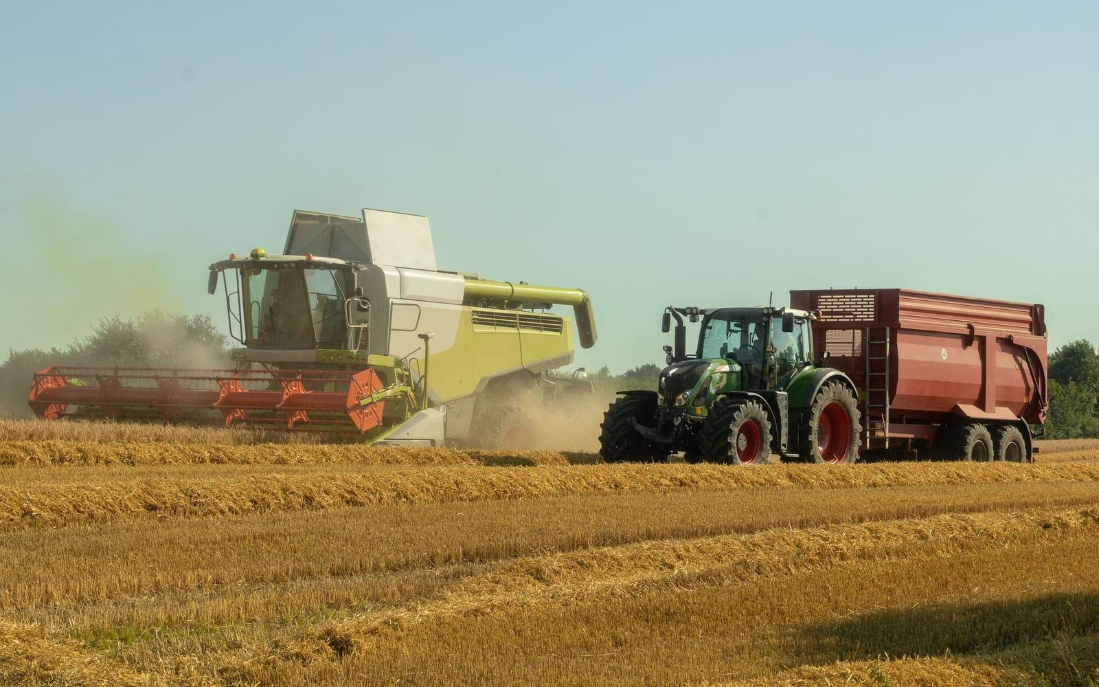 A combine harvester unloading grain into a moving tractor trailer