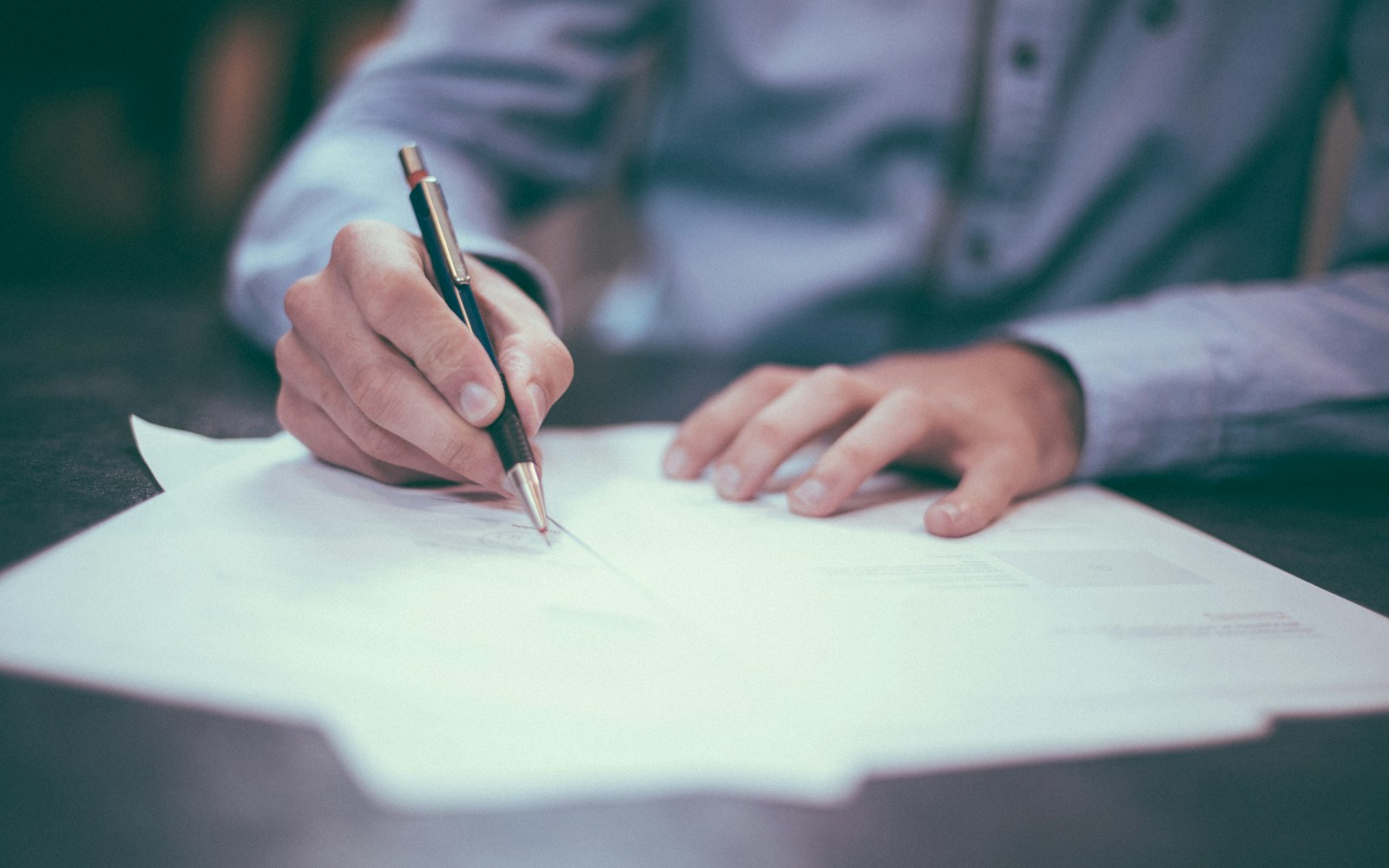 A person signing a printed document at a desk