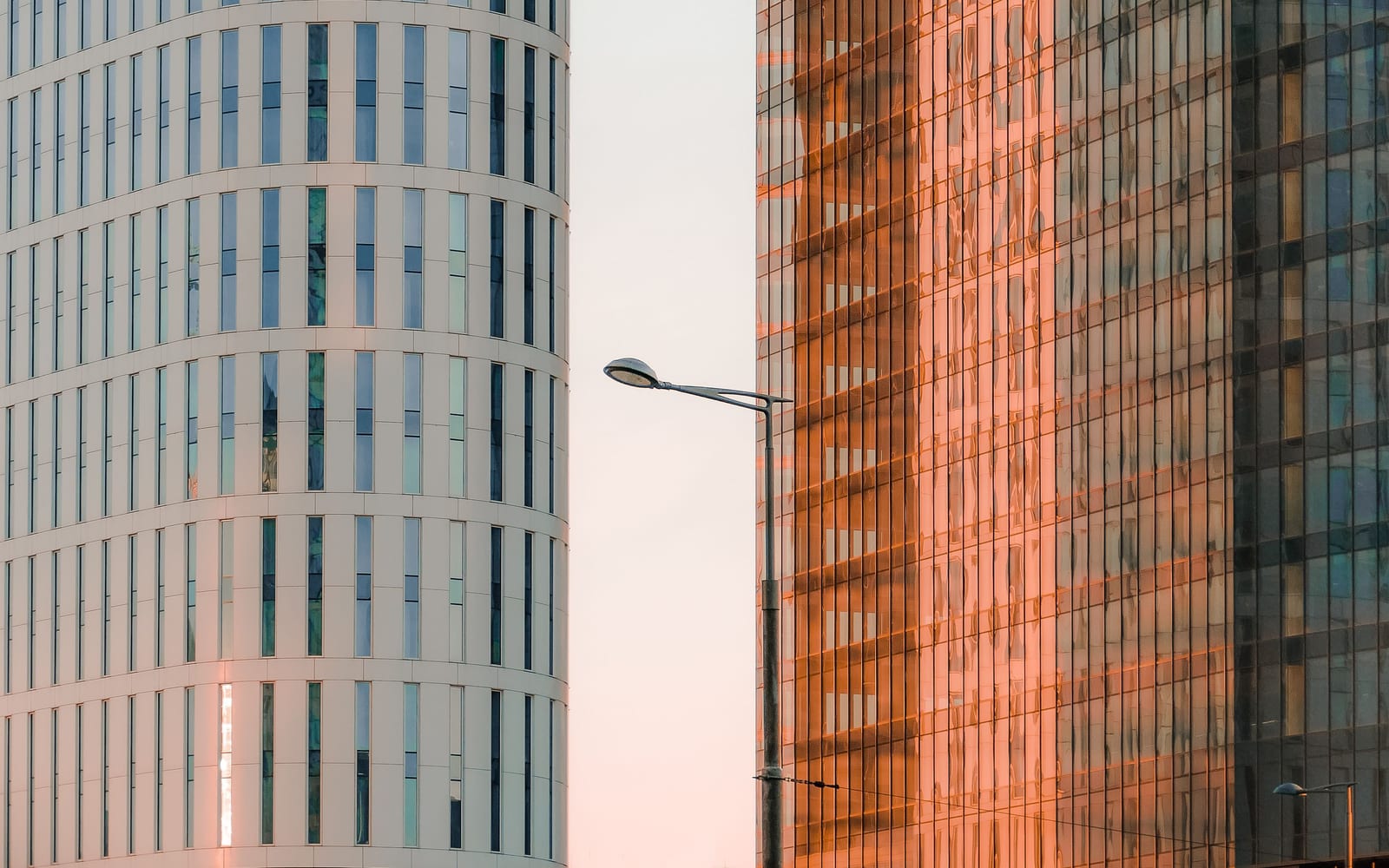 A smooth pale curved tower standing directly against a coloured glass office block