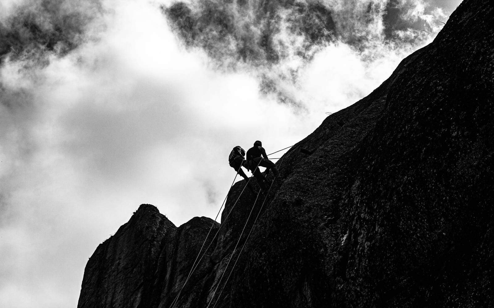 Two climbers roped together high on a rock face, photographed against cloud