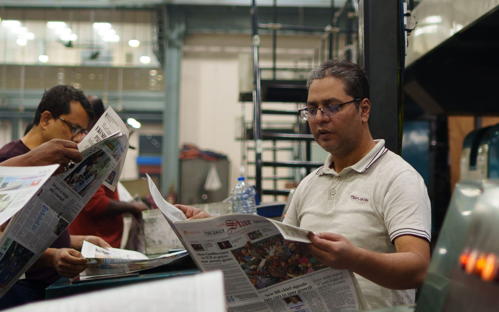 Press workers checking printed sheets as they come off a newspaper press