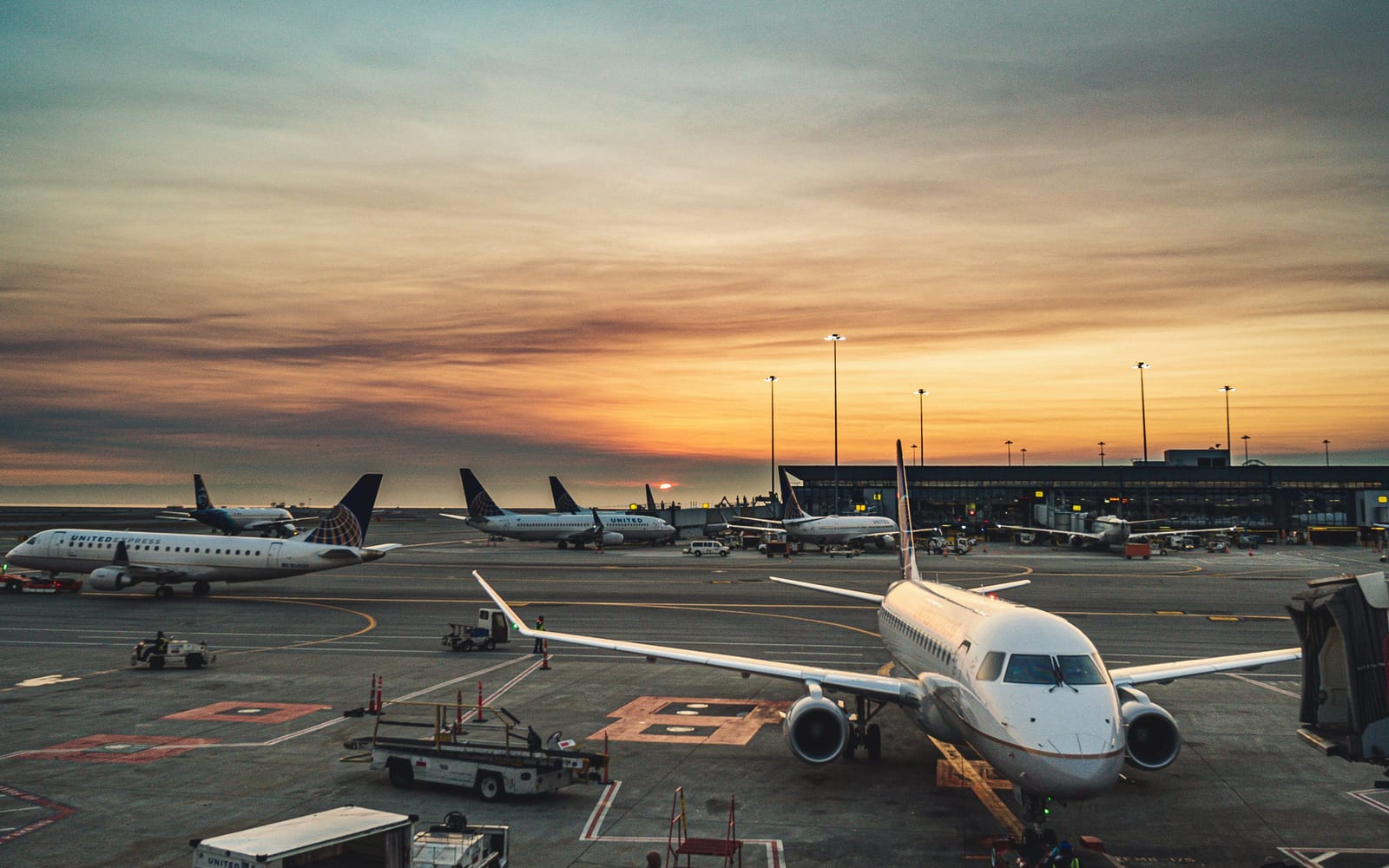 Aircraft at stands on an airport apron with ground vehicles at dusk