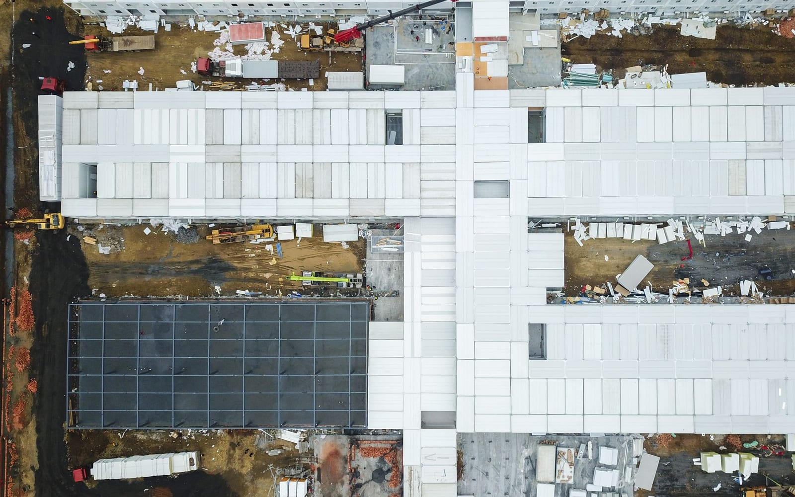 An overhead view of a large building under construction, materials and offcuts spread across the site