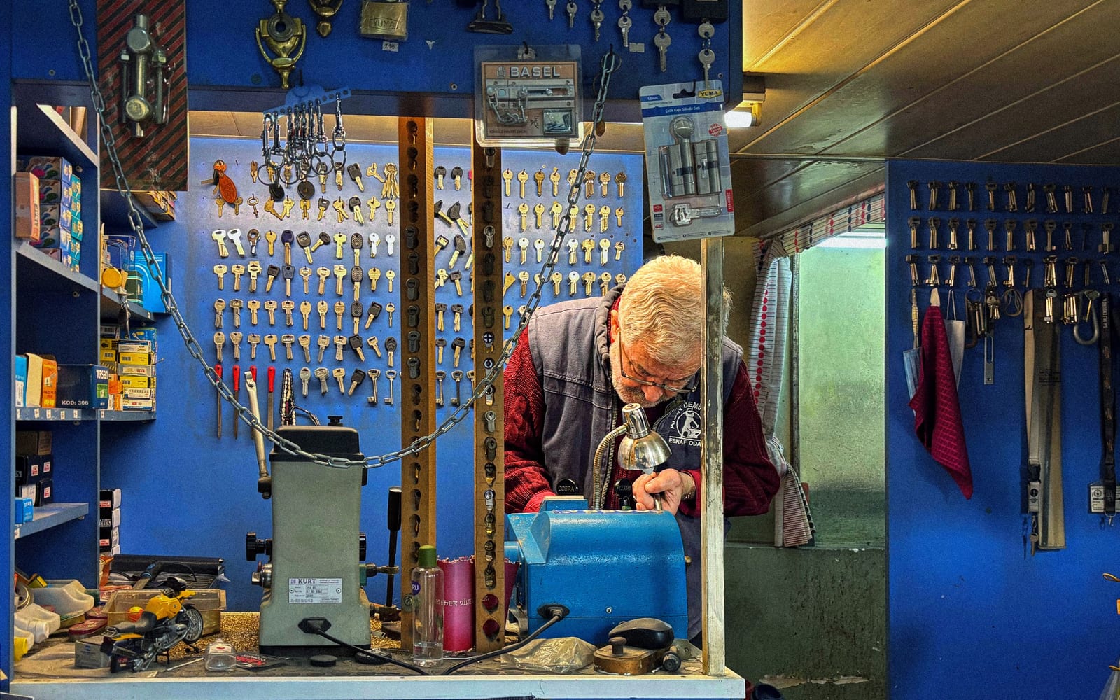 A locksmith at his bench, the walls of the shop hung with hundreds of cut keys