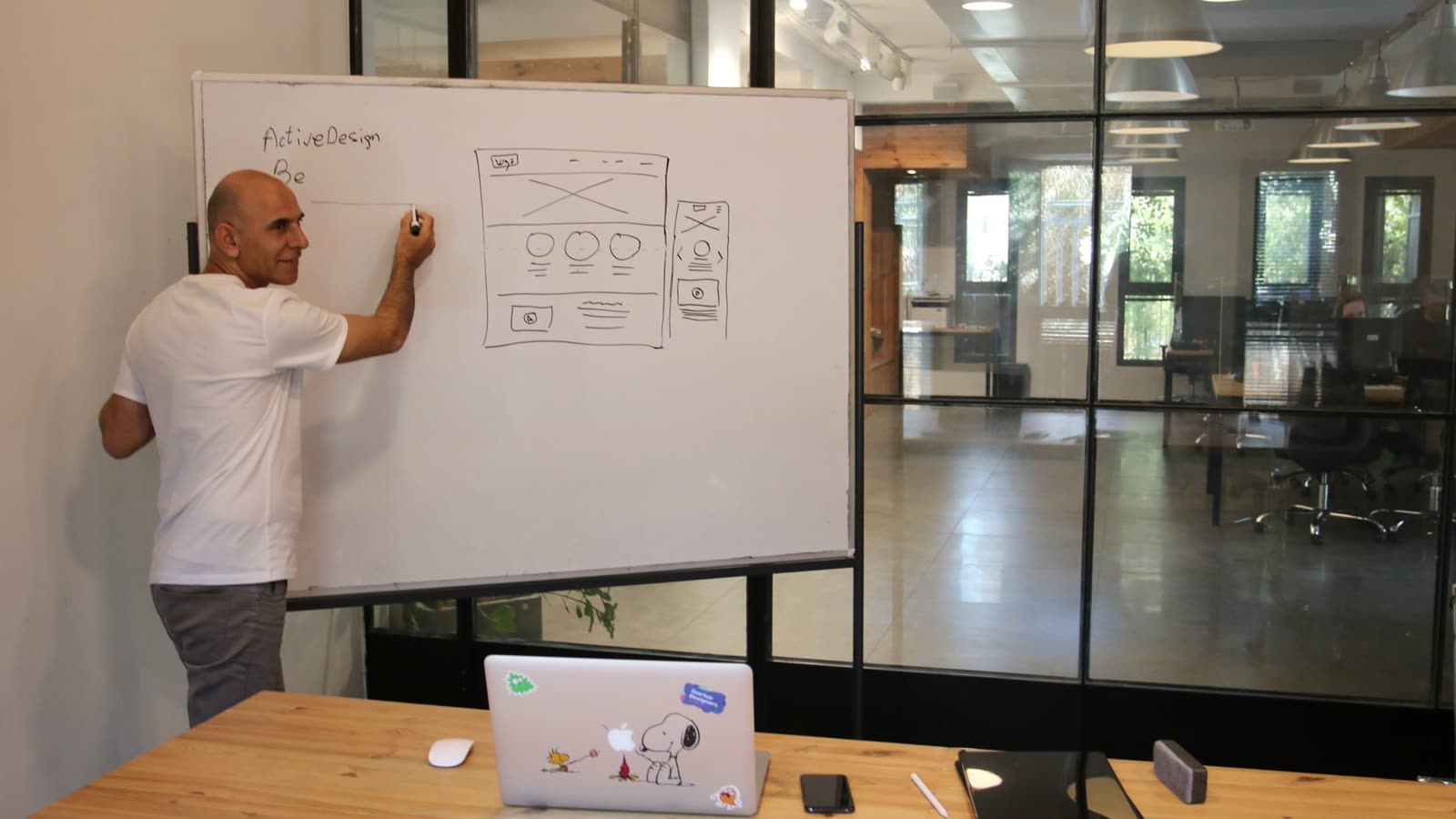 A practitioner sketching a system design on a whiteboard beside a laptop.