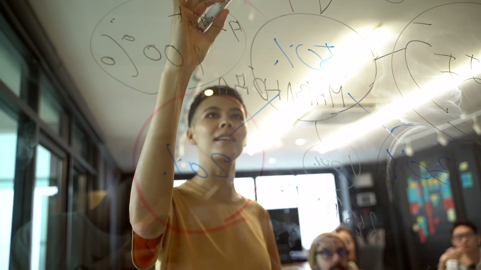 An architect mapping a workflow on a glass wall while the team watches.