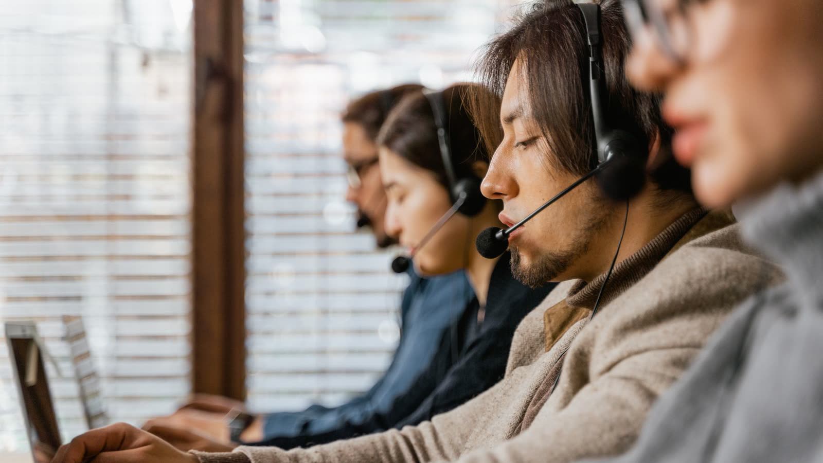 A row of support agents wearing headsets, working side by side on a service floor.