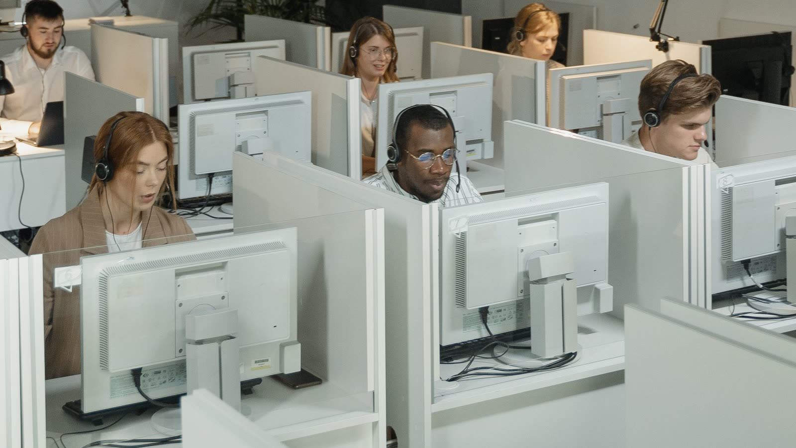 A contact centre floor of agents in headsets working at cubicle workstations.