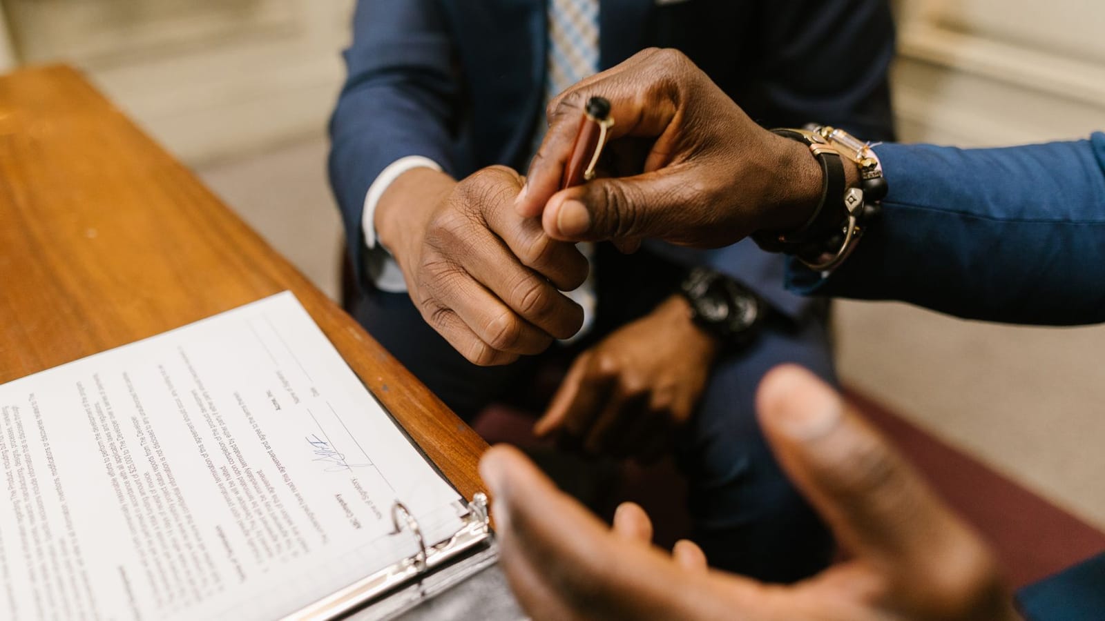 A pen being handed across a desk to sign an agreement.