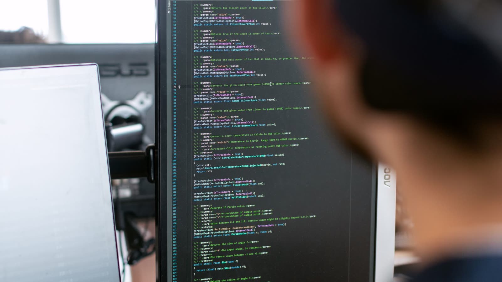 A developer reading through a long file of code on a large monitor.