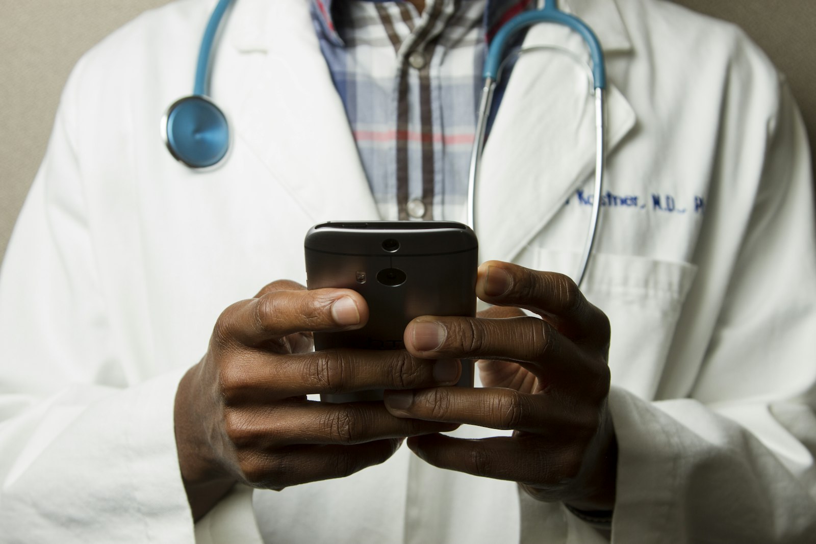 Clinician in a lab coat with a stethoscope using a mobile device for care coordination outside the EHR system of record.