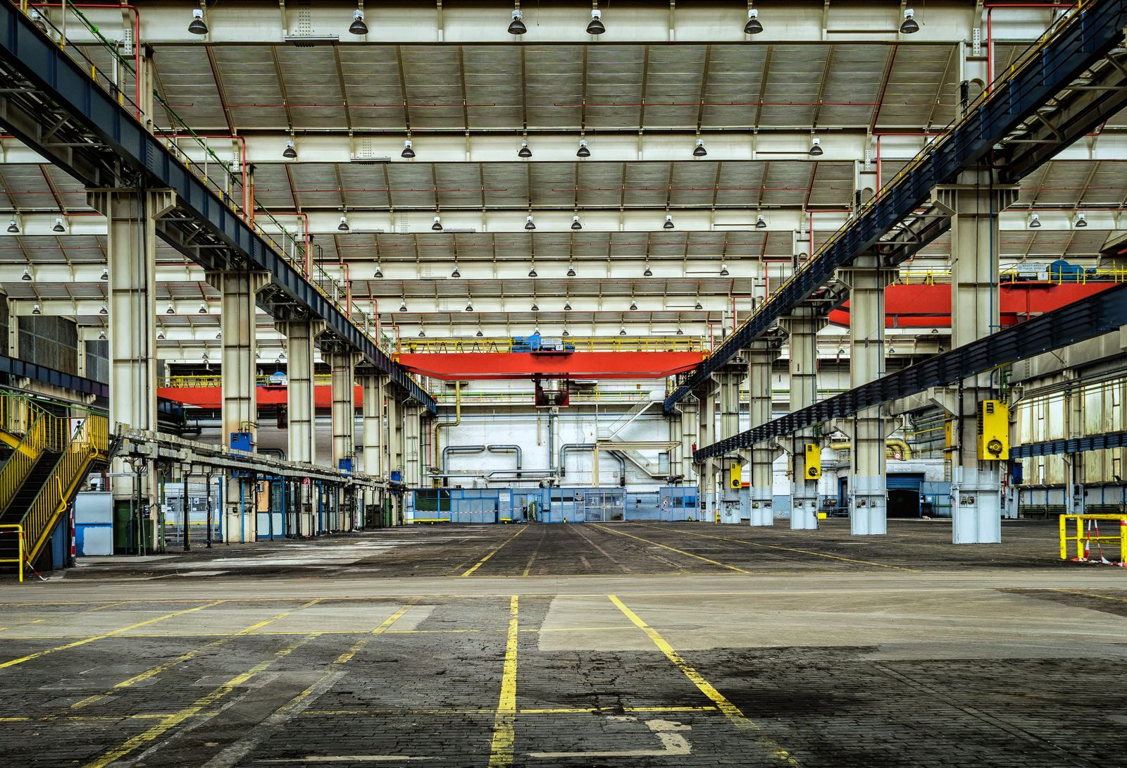 Empty high-bay manufacturing hall with overhead cranes where plant capacity must stay honest with commercial forecasts.
