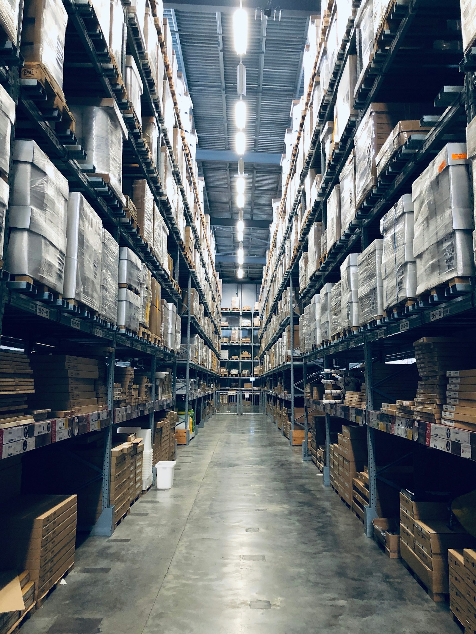 High-bay retail warehouse aisle with pallet inventory, the OMS and stock truth Salesforce must not pretend to replace.
