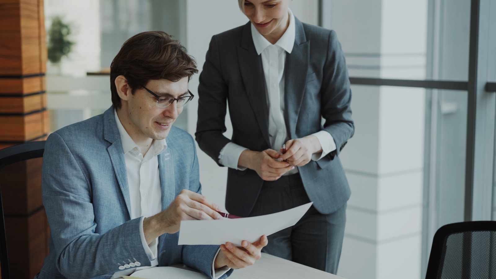 Two colleagues reviewing a document together in an office, one holding a pen ready to sign off.