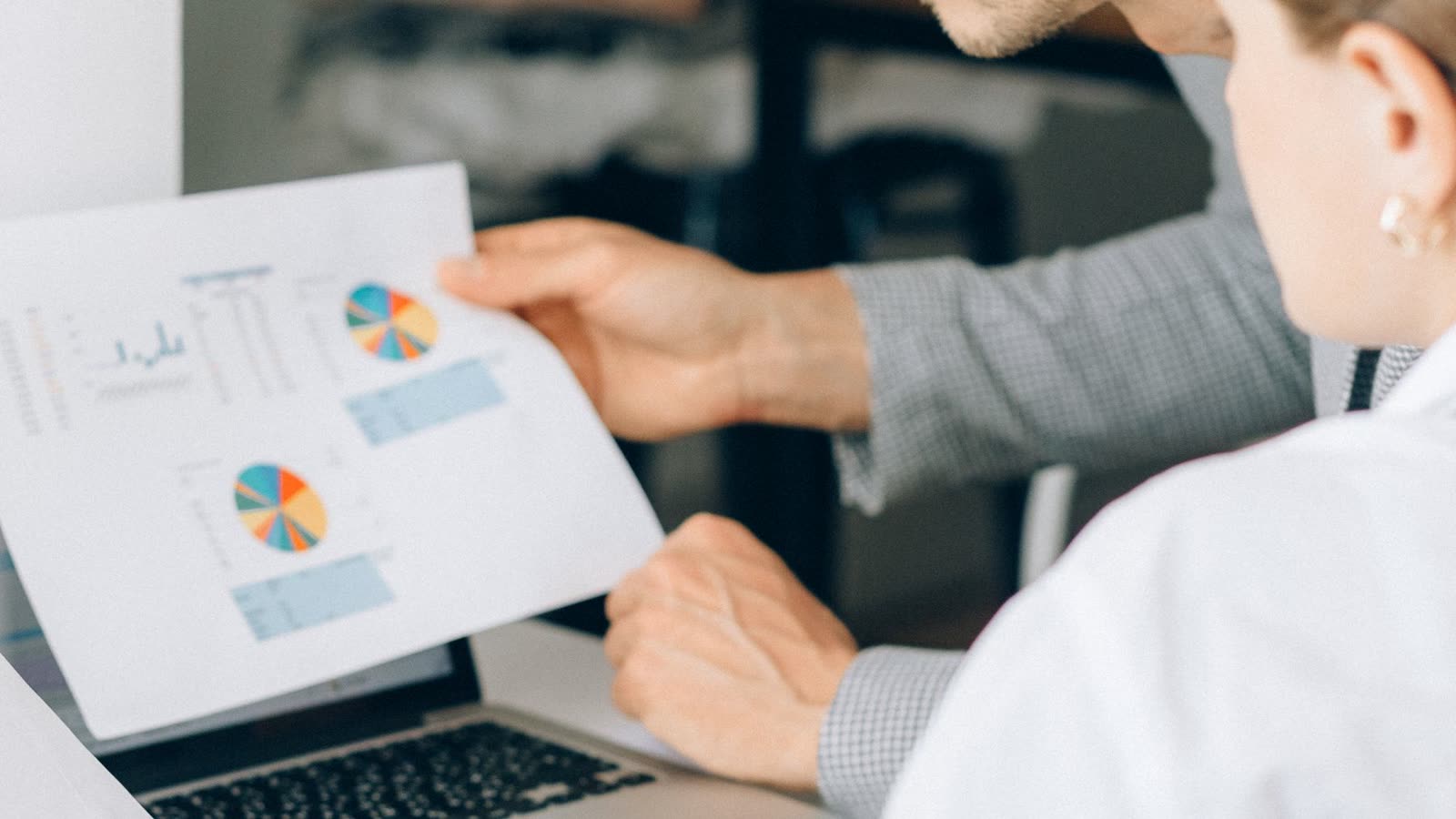 An analyst checking a printed chart against a dashboard on a laptop.